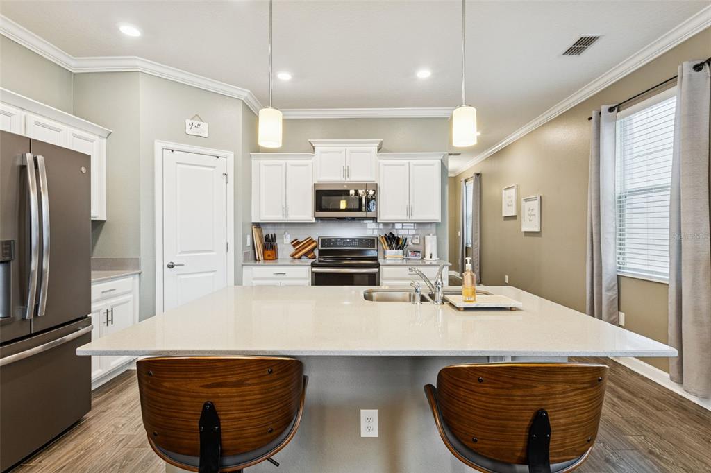 A kitchen features white cabinets, a large quartz island with two stools, and stainless appliances — 10043 SEQUEL ALLEY, WINTER GARDEN, FL