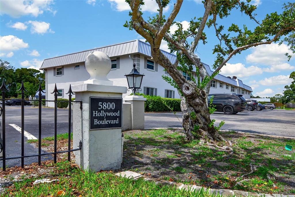 A white two-story building stands behind a stone pillar with a street address sign — 5800 HOLLYWOOD BOULEVARD UNIT 112, SARASOTA, FL