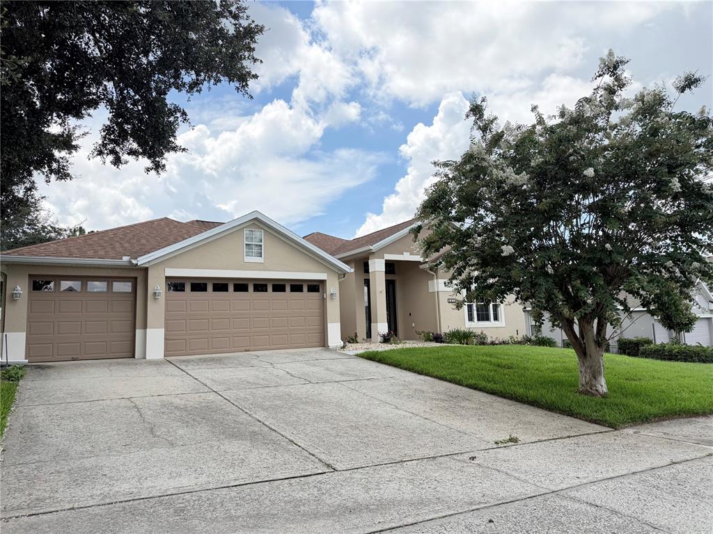 A tan single-story house with a three-car garage and a large flowering tree in front — 2413 PRAIRIE VIEW, WINTER GARDEN, FL
