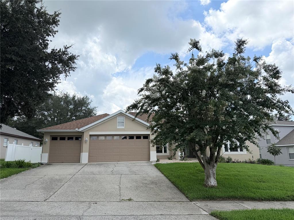 A single-story suburban house with a three-car garage and a large flowering tree — 2413 PRAIRIE VIEW, WINTER GARDEN, FL