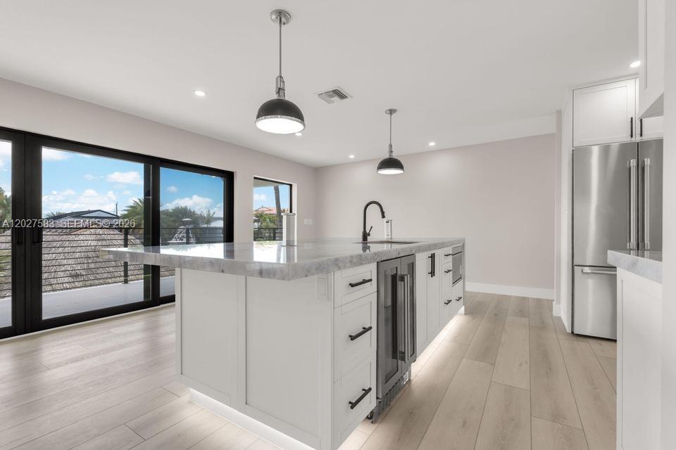 A modern kitchen features a white island with a stone countertop, stainless appliances, and pendant lighting — KEY LARGO, FL