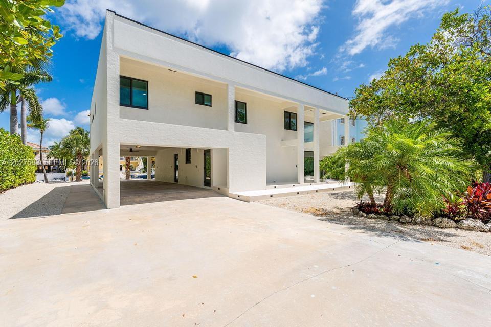 A modern two-story white house features a ground-level carport and a large concrete driveway — KEY LARGO, FL