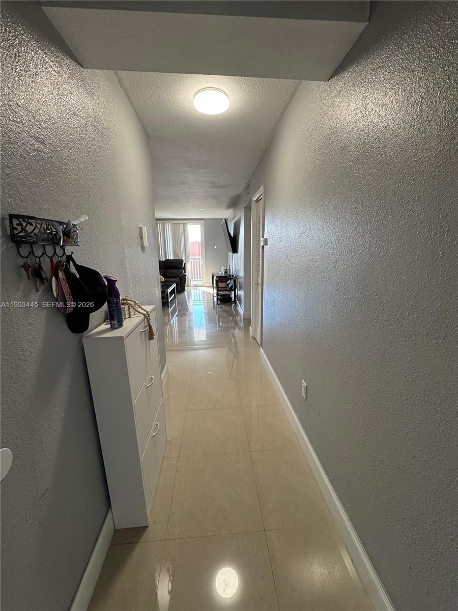 A hallway with light-colored tile flooring leads toward a living area with a balcony — 6960 Miami Gardens Dr # 516, Hialeah FL 33015, HIALEAH, FL