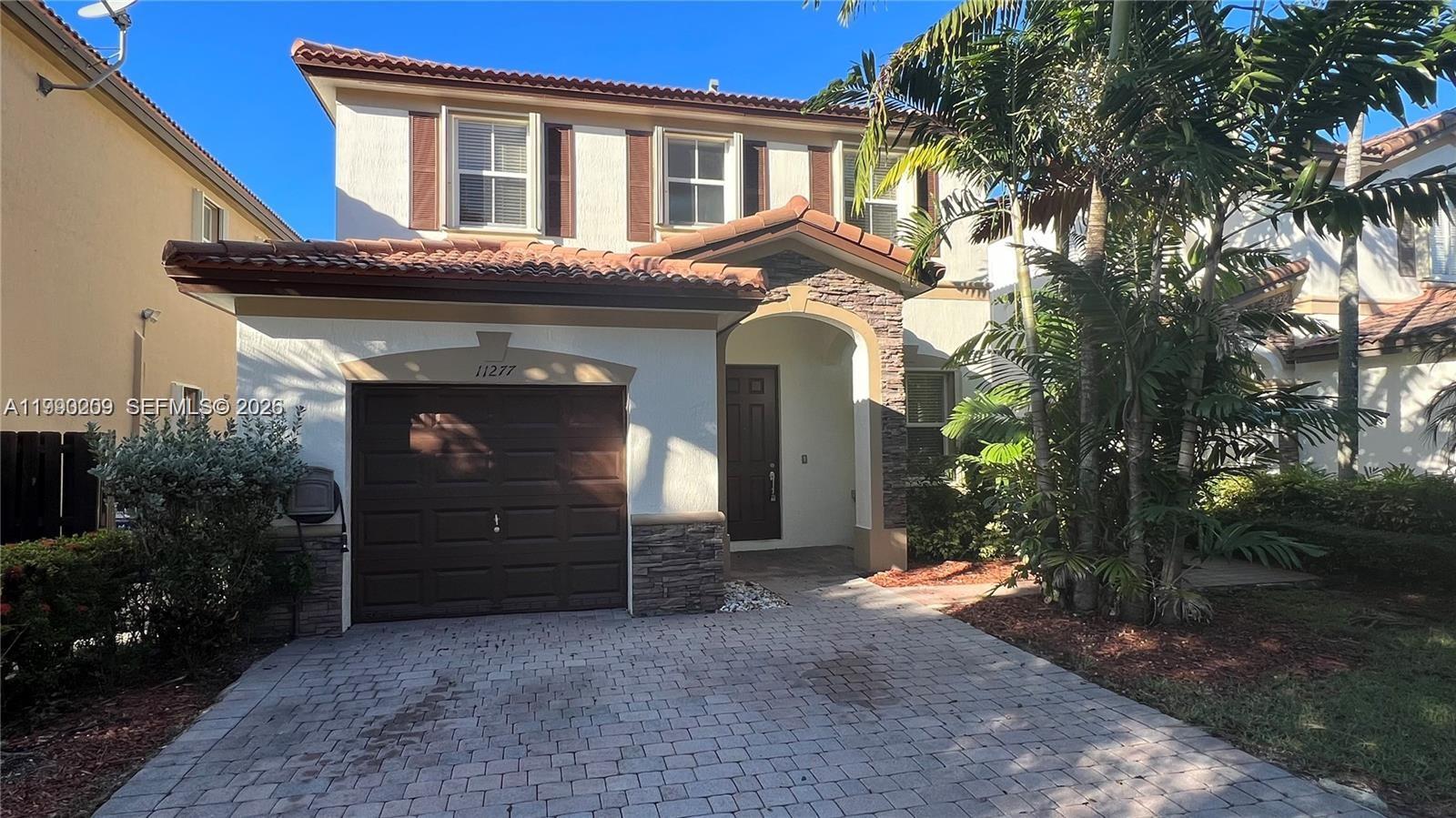 A two-story house features a brown garage door, stone accents, and a paved driveway — 11277 NW 44th Ter, Doral FL 33178, DORAL, FL