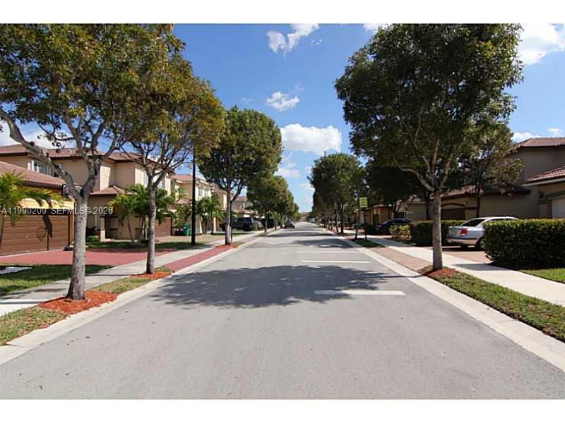 A paved residential street is lined with two-story houses, manicured hedges, and mature trees — 11277 NW 44th Ter, Doral FL 33178, DORAL, FL
