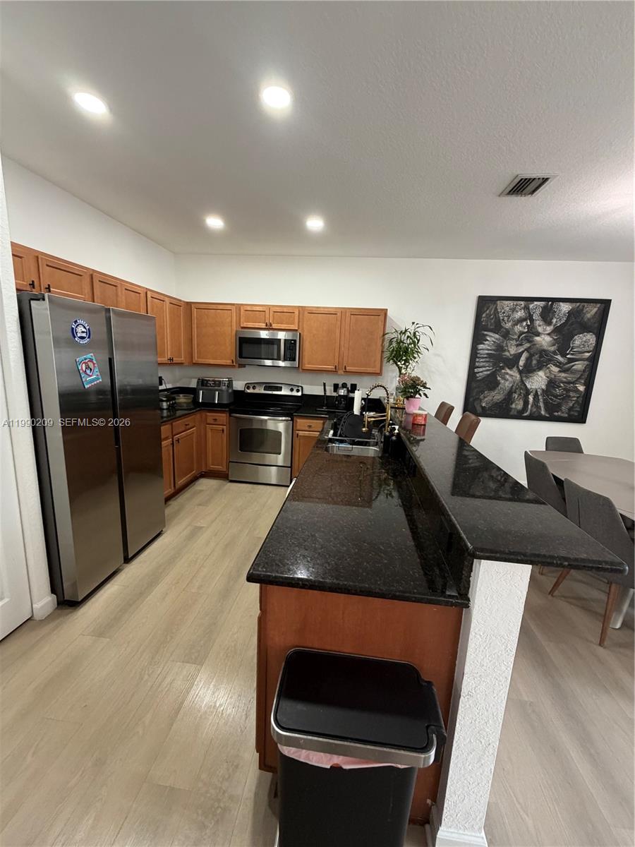 A kitchen features wood cabinets, black granite countertops, stainless steel appliances, and light wood flooring — 11277 NW 44th Ter, Doral FL 33178, DORAL, FL