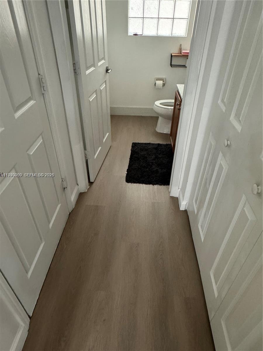 A narrow hallway with light wood-look flooring leads to a small bathroom with a toilet — 11277 NW 44th Ter, Doral FL 33178, DORAL, FL