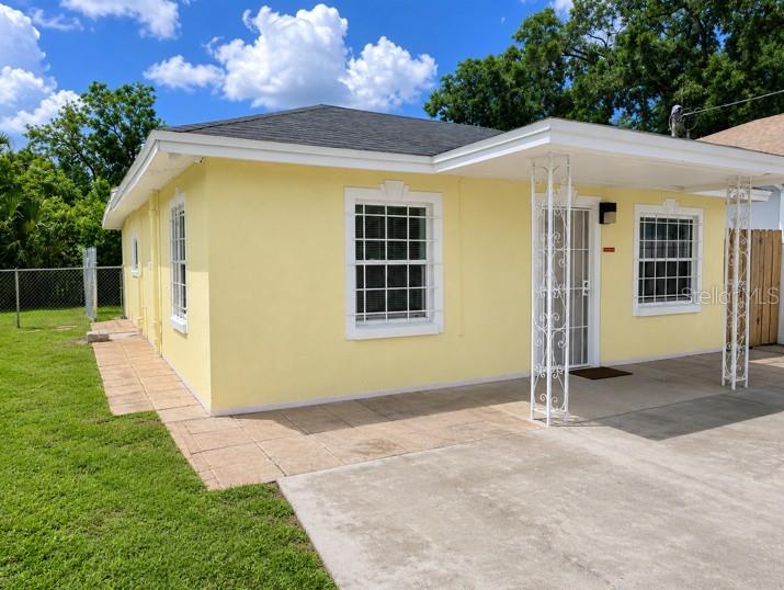 A yellow single-story house features a concrete driveway, a covered porch, and white-framed windows — 1807 E WATERS AVENUE, TAMPA, FL