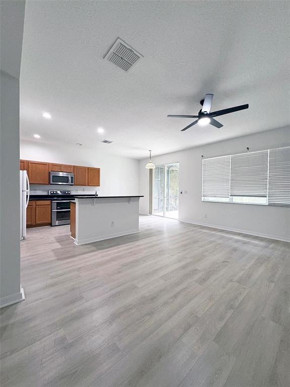 An empty living room features light wood-look flooring, white walls, a ceiling fan, and windows — 654 KETTERING ROAD, DAVENPORT, FL