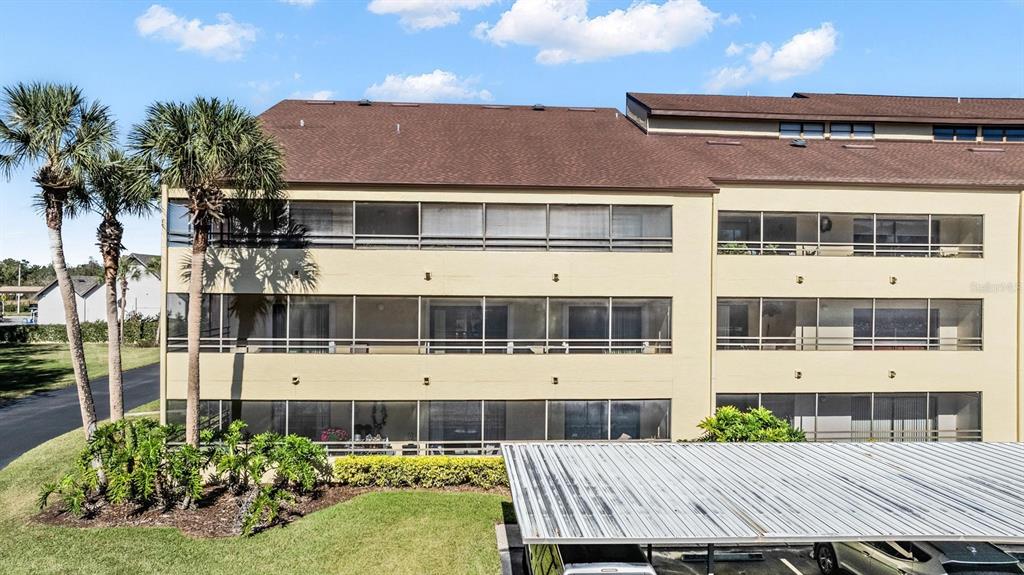 A three-story apartment building with screened balconies and a metal-roofed carport in the foreground — 13612 S VILLAGE DRIVE UNIT 5212, TAMPA, FL