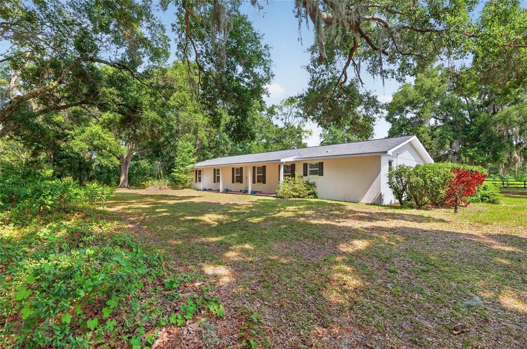 A single-story house with a light-colored exterior sits on a grassy lot among large trees — 7555 SW 77TH PLACE, OCALA, FL