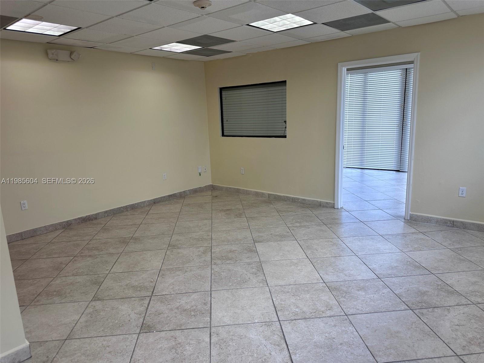 An empty office space features beige walls, tiled flooring, a small window, and drop ceilings — 5455 SW 8 ST # 200, Miami FL 33134, MIAMI, FL
