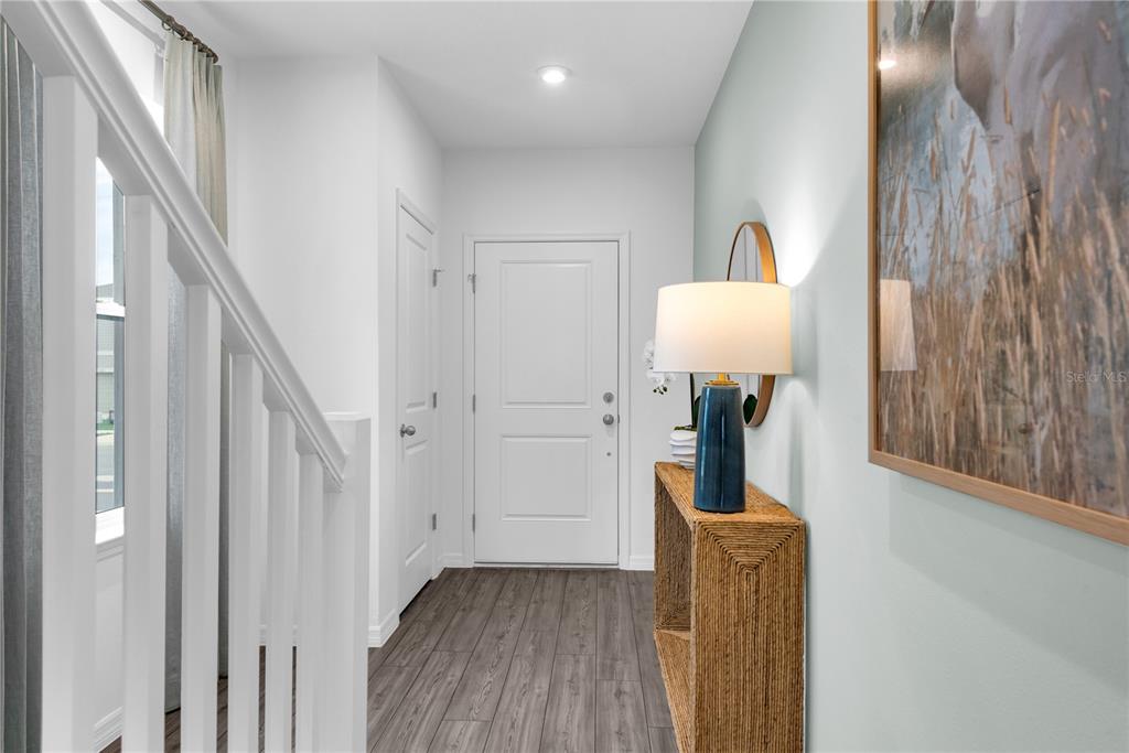 A bright entryway features wood-look flooring, a white staircase railing, and a console table — 3008 JESSAMINE DRIVE, TAVARES, FL
