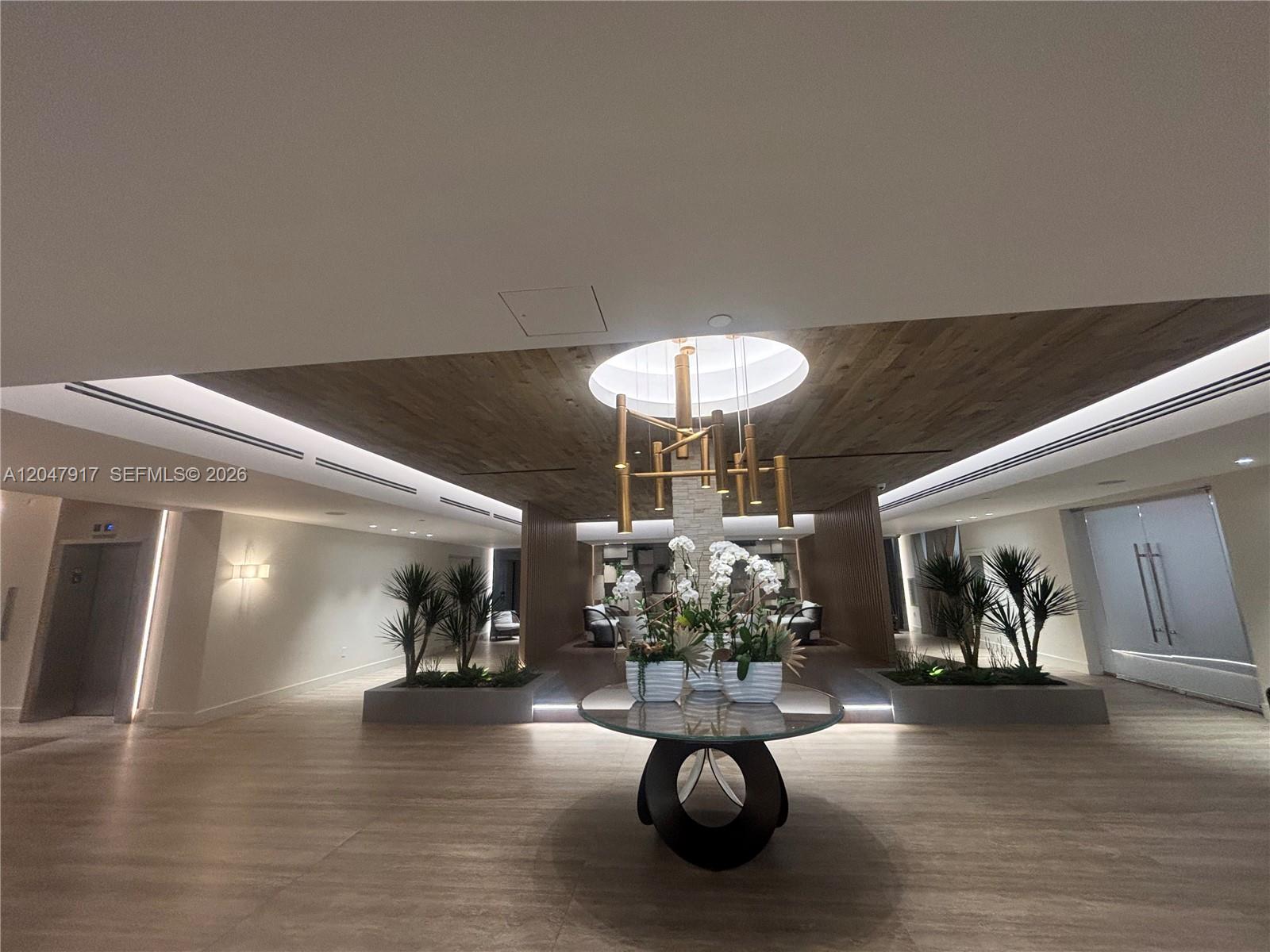 A modern lobby features a circular glass table, a gold chandelier, and indoor planters — 2301 Collins Ave # 833, Miami Beach FL 33139, MIAMI BEACH, FL