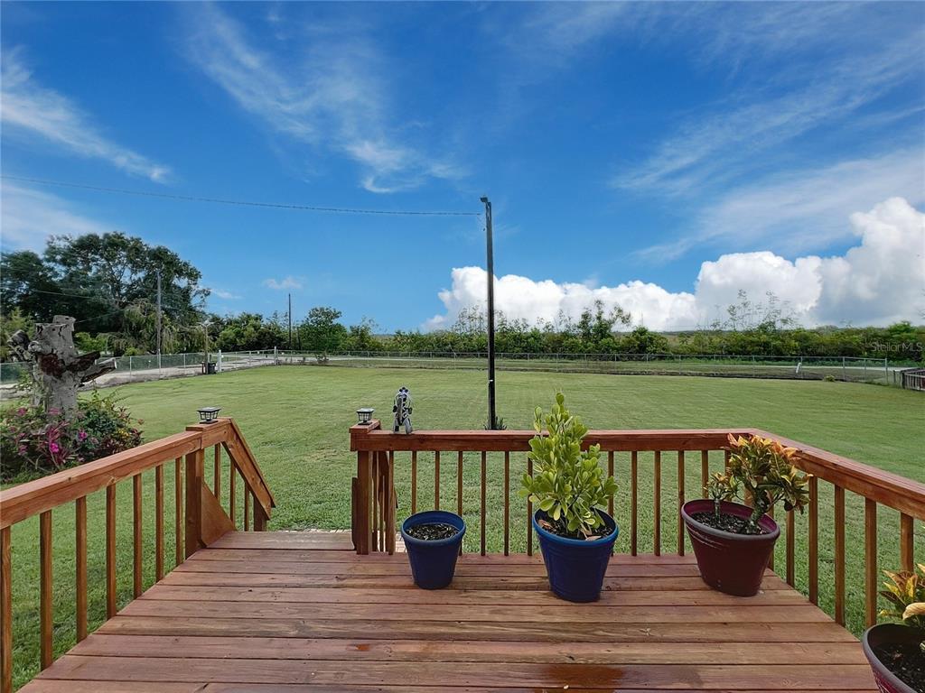 A wooden deck with potted plants overlooks a large grassy backyard under a blue sky — 3710 KANDY LANE, HAINES CITY, FL