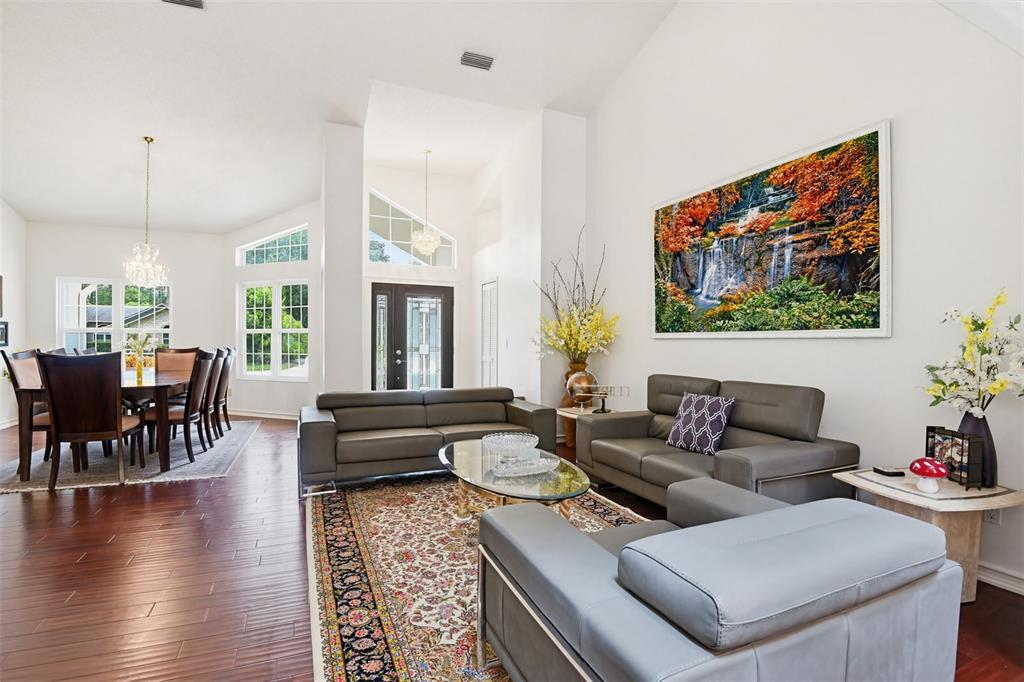 A living room and dining area with hardwood floors, vaulted ceilings, and gray leather furniture — 114 SHADOWCREEK WAY, ORMOND BEACH, FL