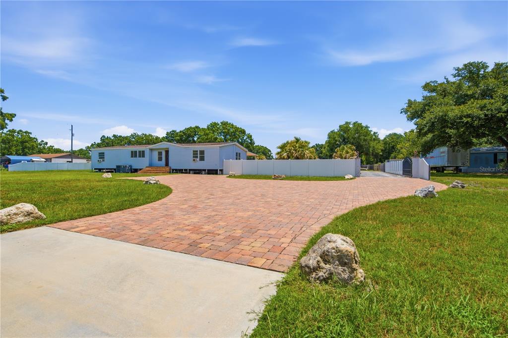 A light blue manufactured home sits behind a large, curved paver driveway and white fence — 6502 FIVE ACRE ROAD, PLANT CITY, FL