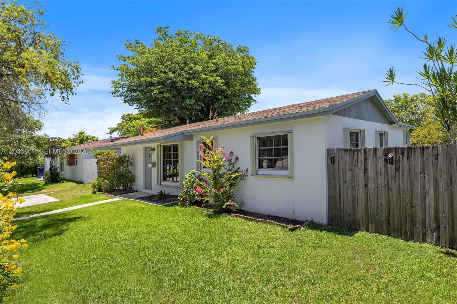 A white single-story house with a wooden fence and a green lawn under blue skies — 9971 SW 156th Ter, Miami FL 33157, MIAMI, FL