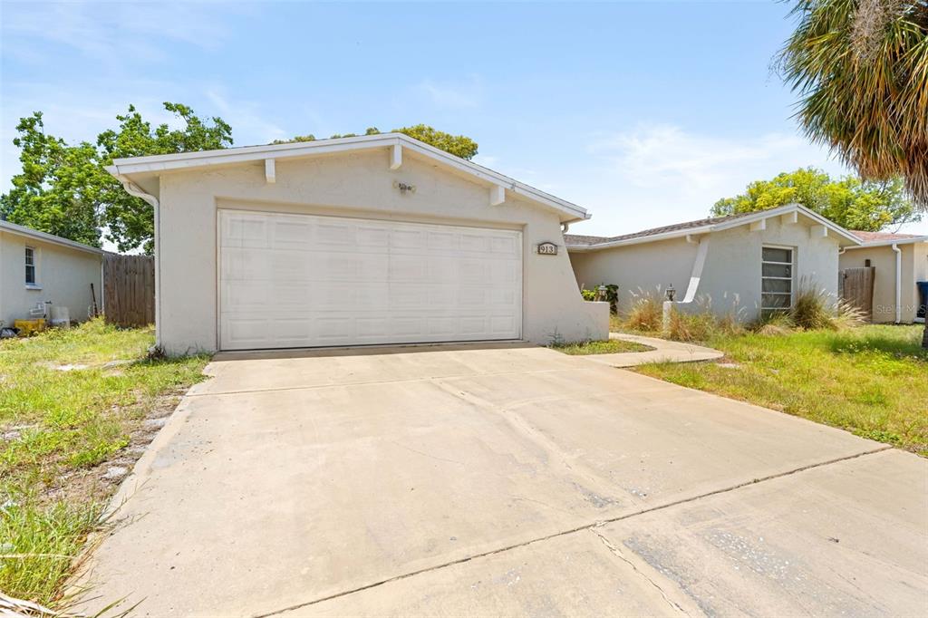 A single-story house with a beige stucco exterior, a two-car garage, and a concrete driveway — 9131 HUNT CLUB LANE, PORT RICHEY, FL