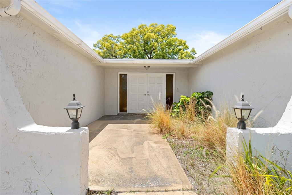 A concrete walkway leads to a white double-door entrance flanked by two outdoor lamps — 9131 HUNT CLUB LANE, PORT RICHEY, FL