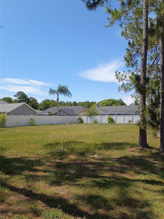 A large, grassy backyard features a white vinyl fence and several pine trees — 5142 LA PLATA DRIVE, NEW PORT RICHEY, FL