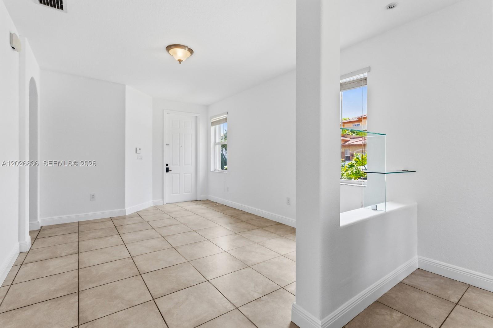 An empty room features white walls, beige tile flooring, a front door, and glass shelving — 8610 NW 110th Ave, Doral FL 33178, DORAL, FL