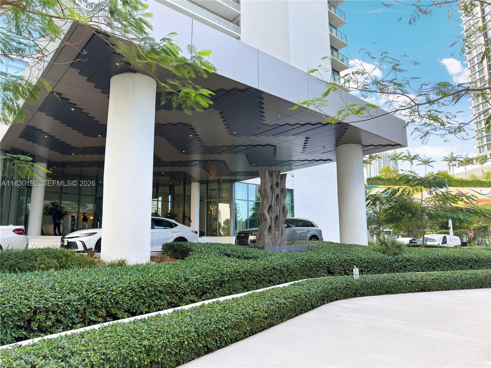 The exterior entrance of a modern building features a large overhang supported by white columns — 650 NE 32nd St # 802, Miami FL 33137, MIAMI, FL