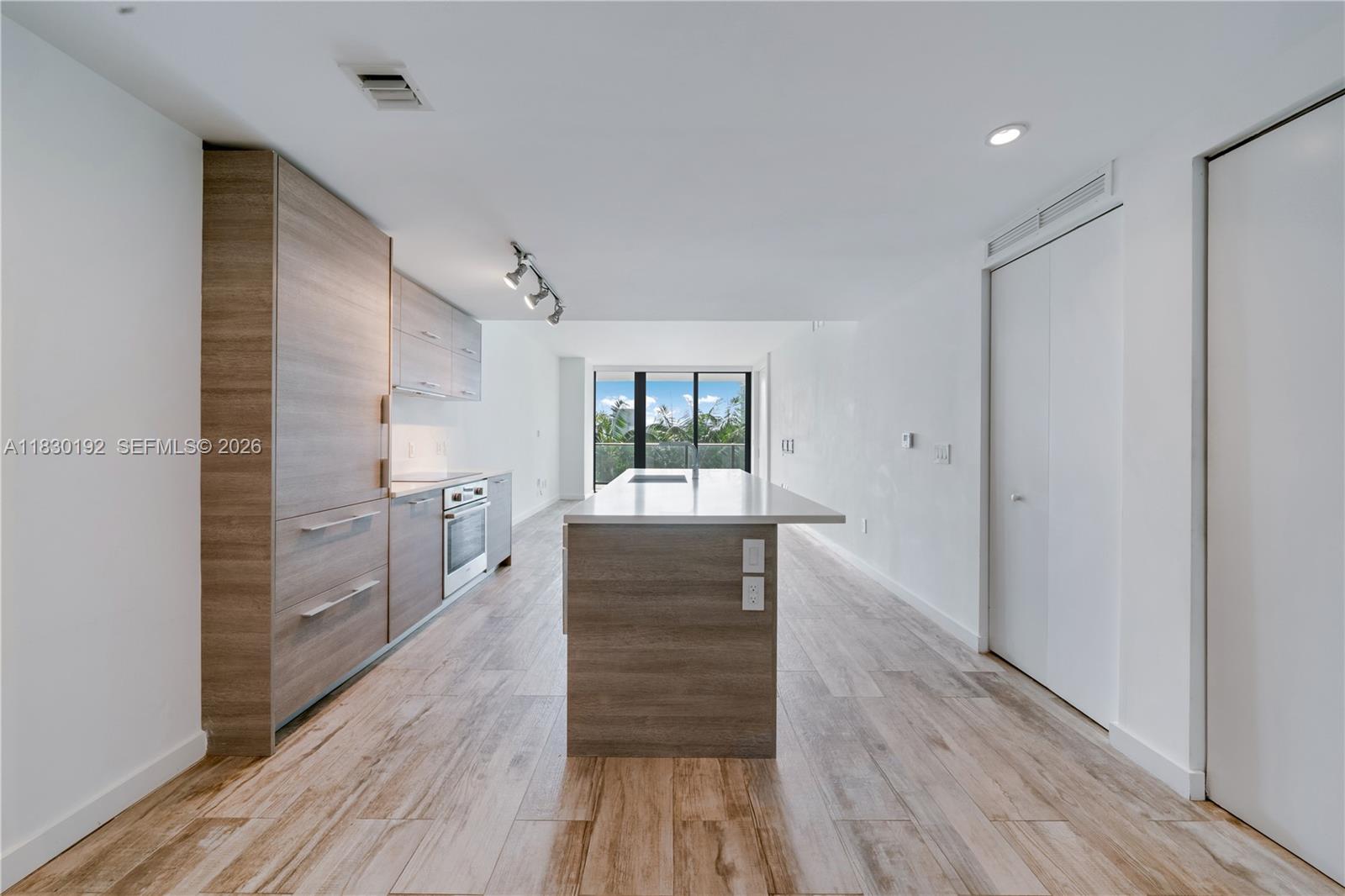 A modern kitchen features wood-grain cabinetry, a central island, and light-colored wood-look flooring — 650 NE 32nd St # 802, Miami FL 33137, MIAMI, FL