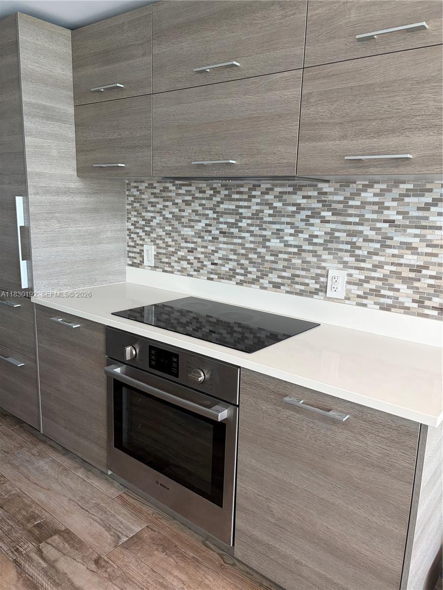 A modern kitchen features wood-grain cabinets, a white countertop, a glass cooktop, and mosaic backsplash — 650 NE 32nd St # 802, Miami FL 33137, MIAMI, FL