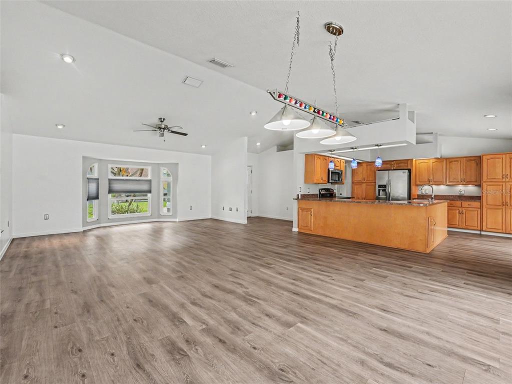 A spacious open-concept living area features wood-look flooring, a kitchen island, and a bay window — 6736 NELLS WAY, LAKELAND, FL