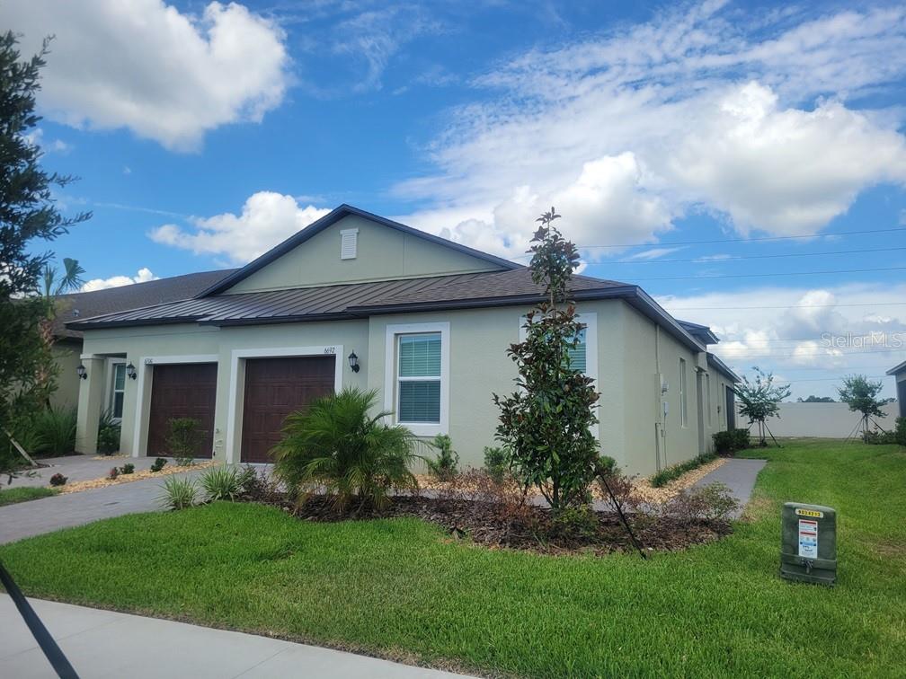A single-story duplex with a light green exterior, dark metal roof, and two garage doors — 6692 HOMEBOUND WAY, NEW PORT RICHEY, FL