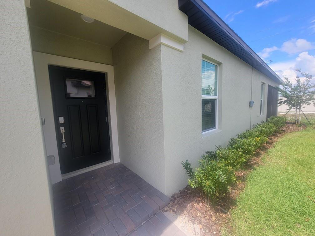 A view of a home exterior featuring a black front door and a paved entryway — 6692 HOMEBOUND WAY, NEW PORT RICHEY, FL