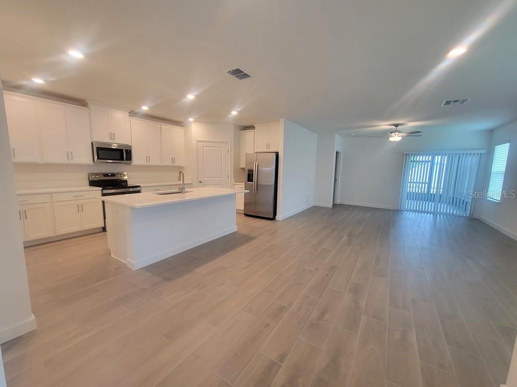 An open-concept kitchen and living area feature white cabinetry, stainless steel appliances, and wood-look flooring — 6692 HOMEBOUND WAY, NEW PORT RICHEY, FL