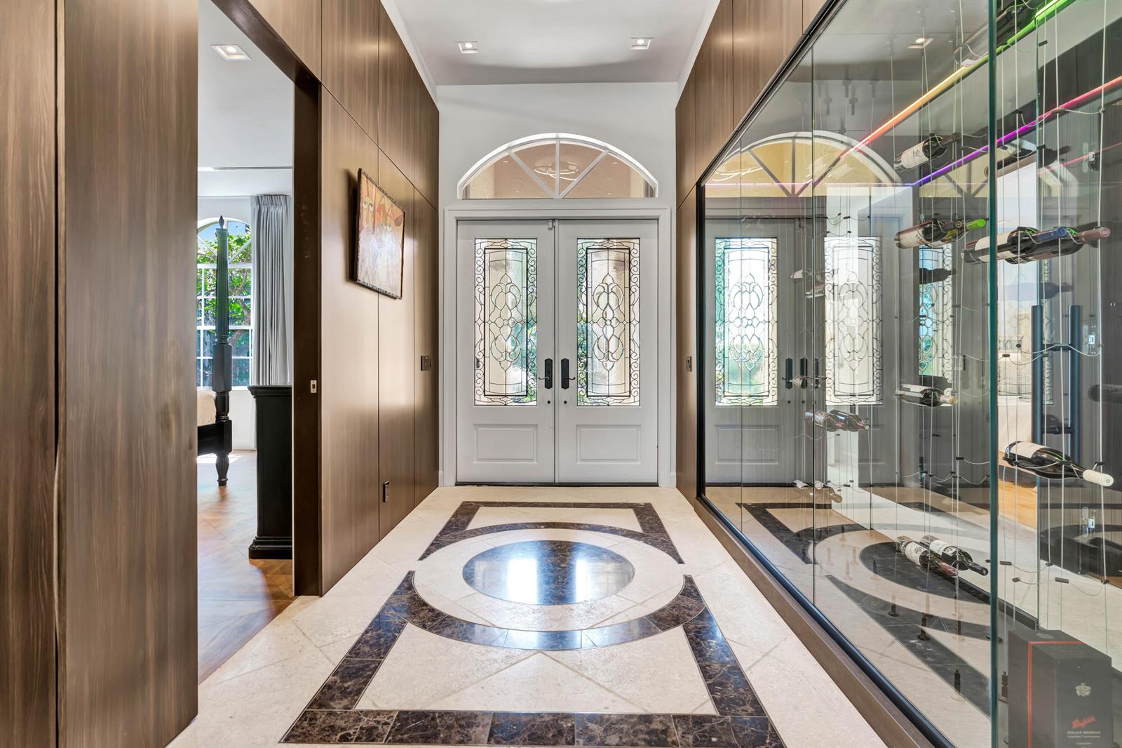 A foyer features a patterned stone floor, double front doors, and a glass-enclosed wine display — 186 Golf Village Boulevard, Jupiter FL 33458, JUPITER, FL