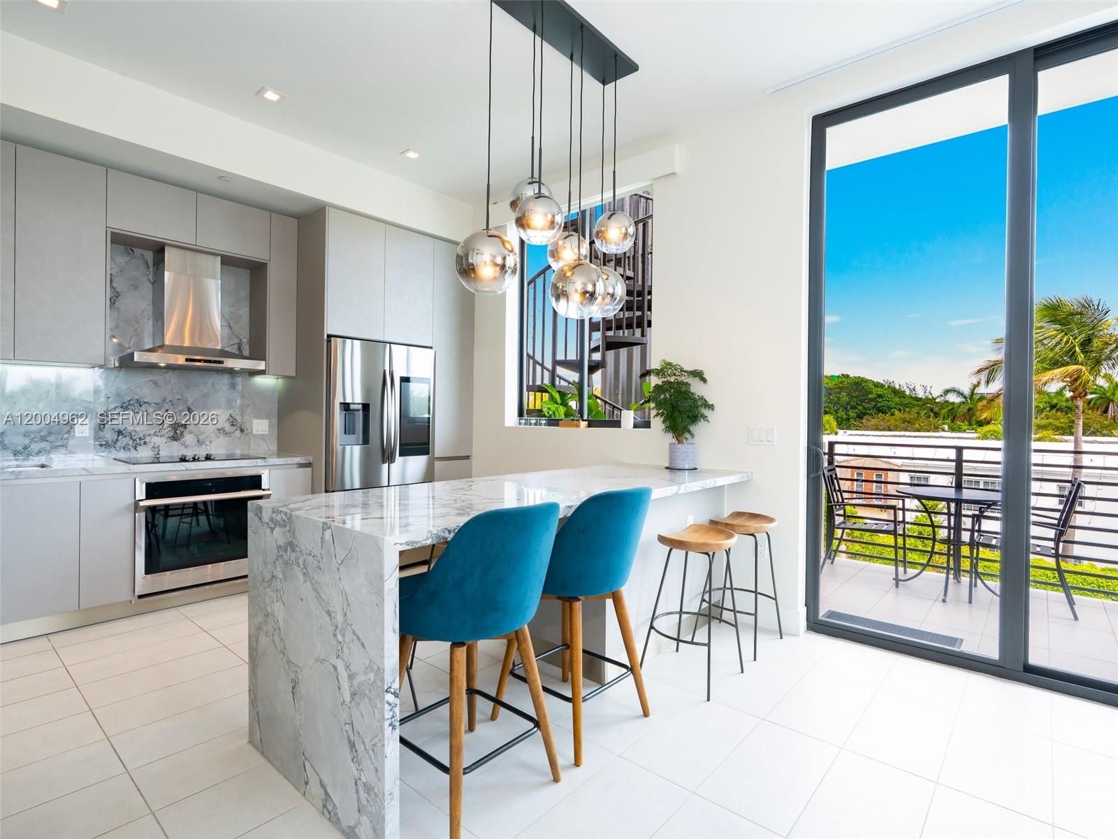A modern kitchen features a marble waterfall island, blue velvet stools, and a balcony view — 1030 15th St # 321, Miami Beach FL 33139, MIAMI BEACH, FL