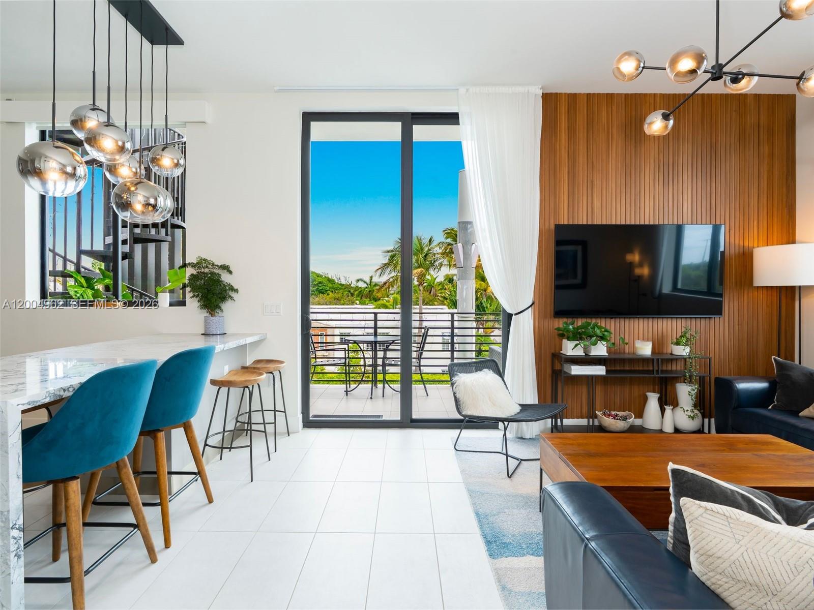 A modern living room and kitchen area features a wood-paneled wall, balcony, and marble island — 1030 15th St # 321, Miami Beach FL 33139, MIAMI BEACH, FL