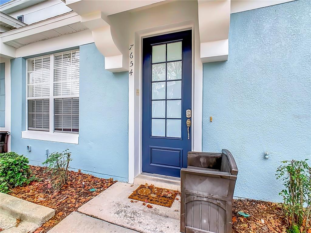 A blue front door with a glass pane sits beside a window on a house — 7654 OTTERSPOOL STREET, KISSIMMEE, FL