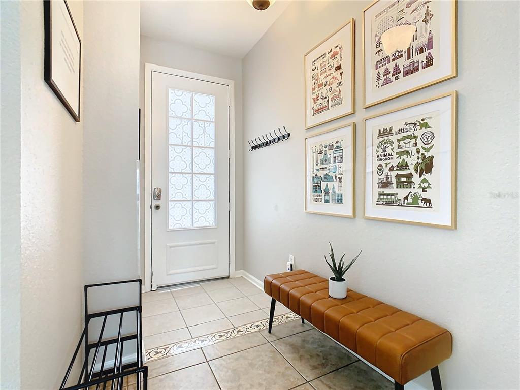 An entryway features a white front door, a brown leather bench, and four framed prints — 7654 OTTERSPOOL STREET, KISSIMMEE, FL