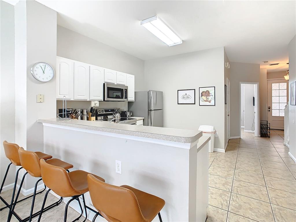 A kitchen with white cabinets, stainless steel appliances, and a breakfast bar with three stools — 7654 OTTERSPOOL STREET, KISSIMMEE, FL
