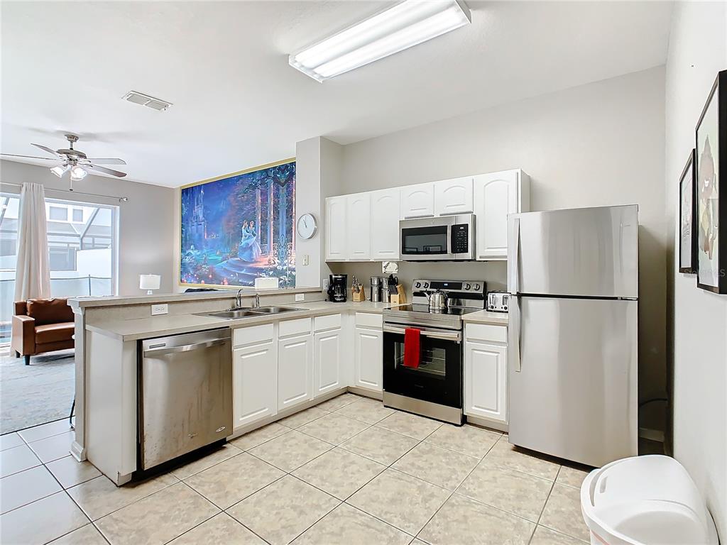 A kitchen with white cabinets, stainless steel appliances, and tile flooring overlooks a living area — 7654 OTTERSPOOL STREET, KISSIMMEE, FL