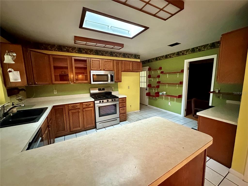 A kitchen features wood cabinets, stainless steel appliances, green walls, and a central island — 9138 LESWOOD STREET, ORLANDO, FL