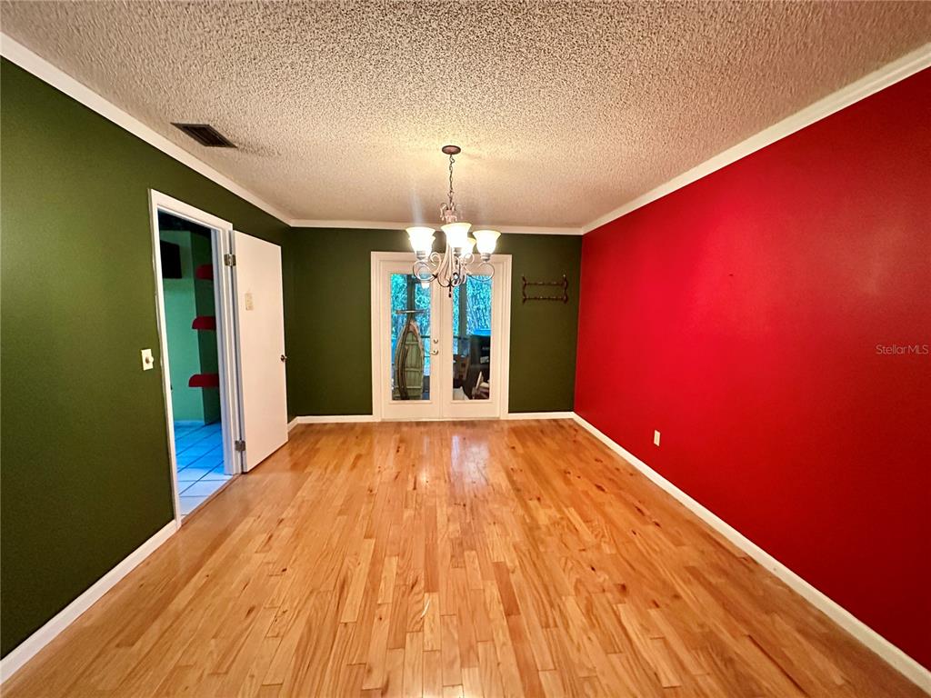 A dining room features hardwood floors, a chandelier, and walls painted in green and red — 9138 LESWOOD STREET, ORLANDO, FL