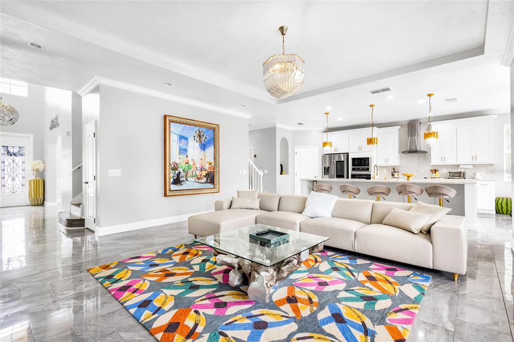 A modern open-concept living room features a large sectional sofa, colorful area rug, and kitchen — 8631 TERRACE PINES COURT, ORLANDO, FL
