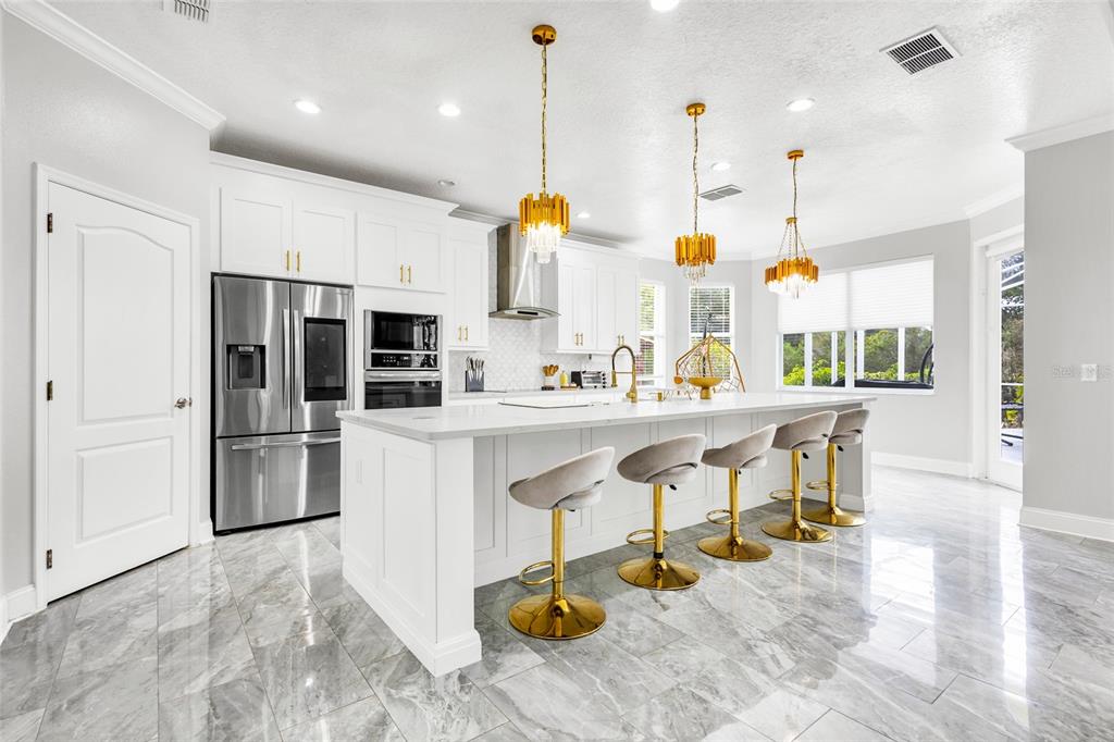 A modern white kitchen features a large island with gold-accented bar stools and marble flooring — 8631 TERRACE PINES COURT, ORLANDO, FL