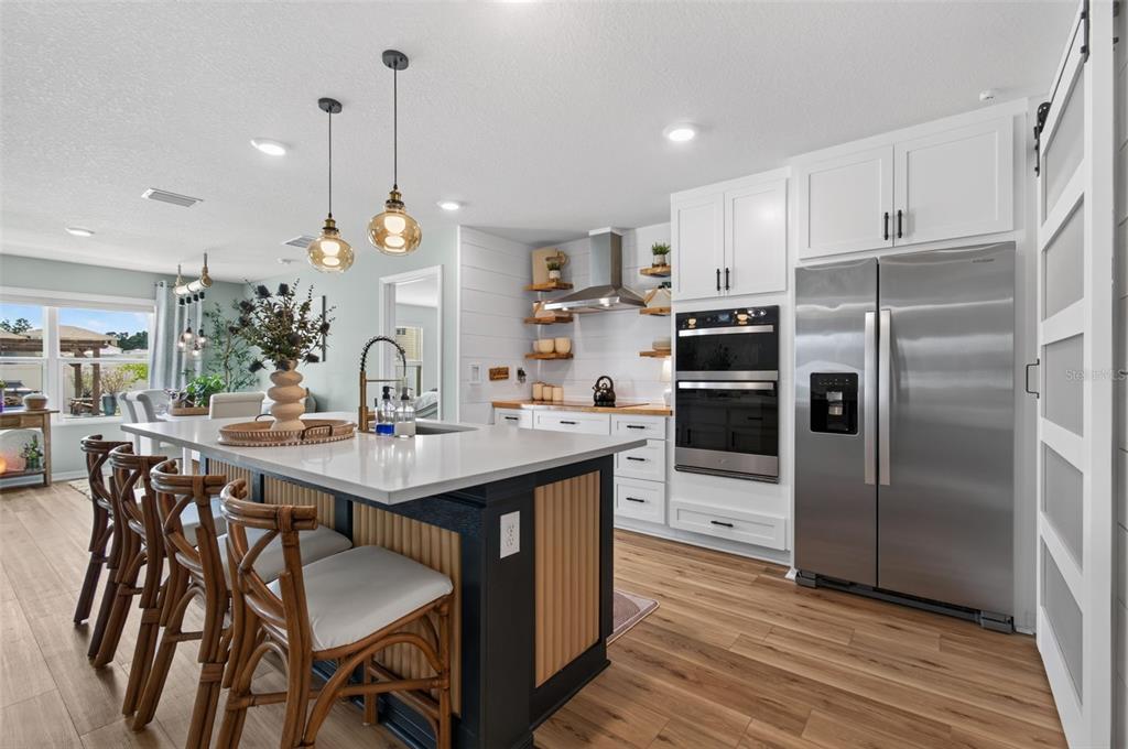 A modern kitchen features a dark island with bar seating, white cabinetry, and stainless appliances — 17077 NW 177TH TERRACE, ALACHUA, FL