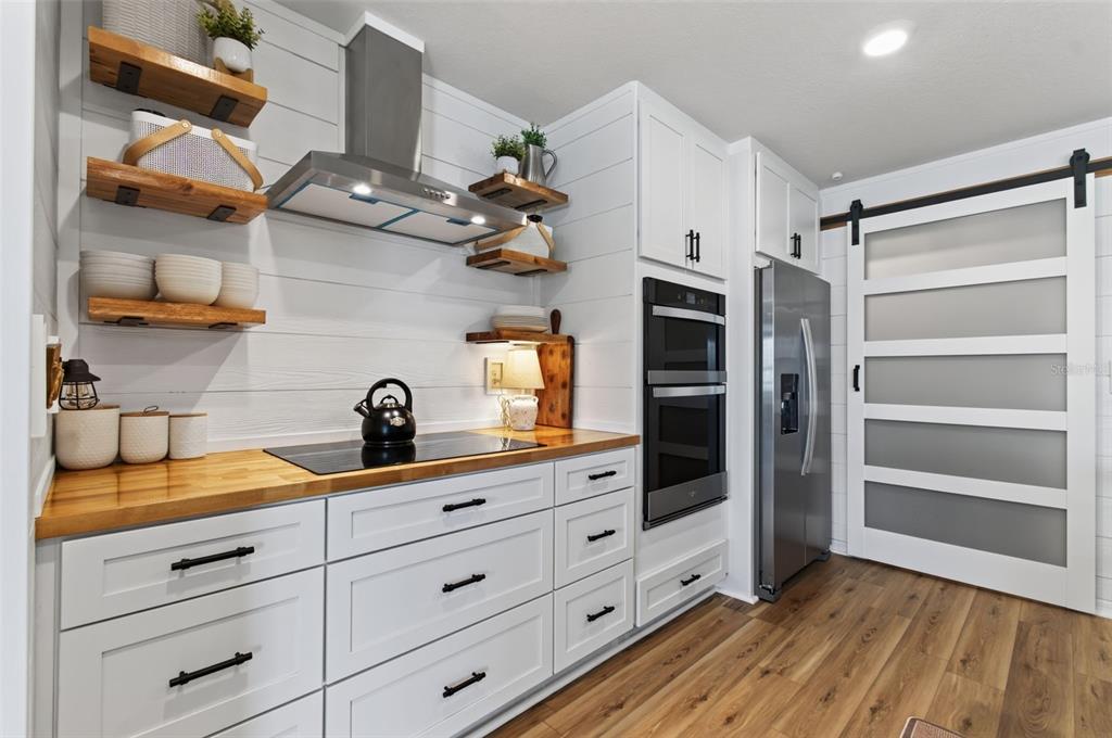 A modern kitchen features white cabinets, wood countertops, open shelving, and a sliding barn door — 17077 NW 177TH TERRACE, ALACHUA, FL