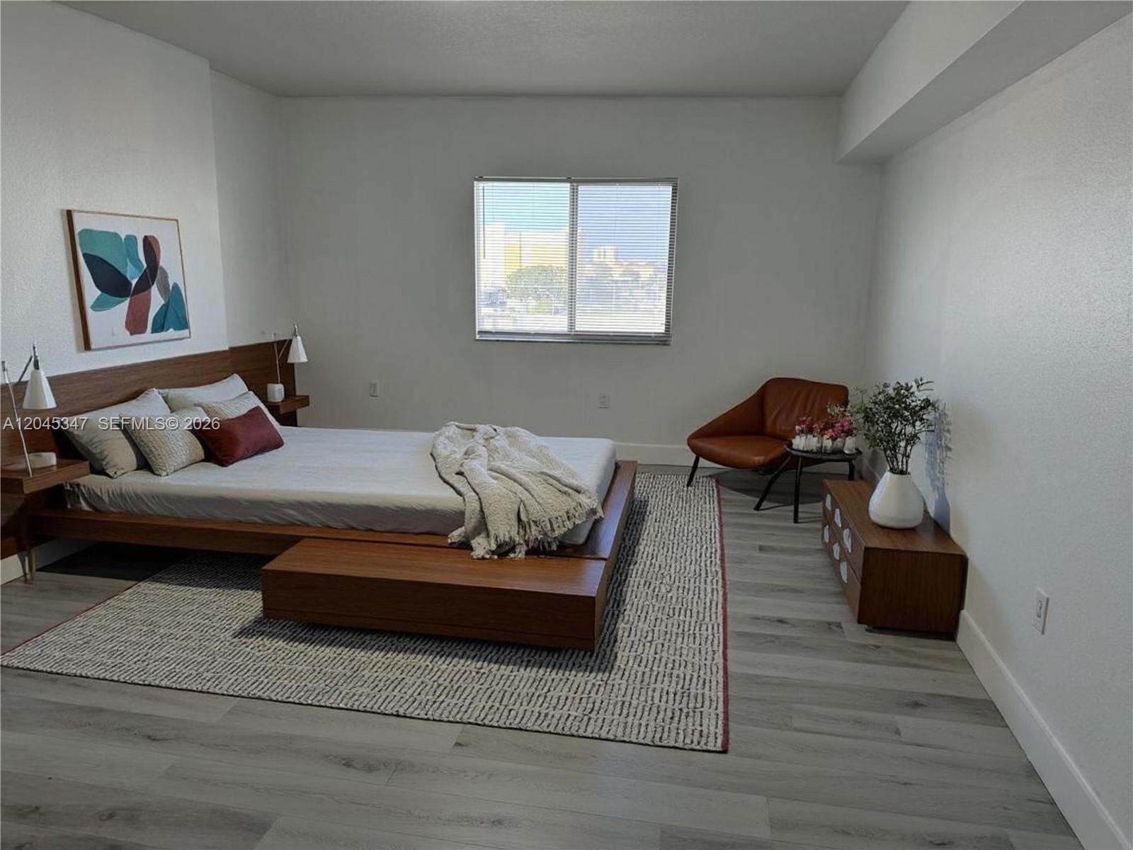 A bedroom features a wooden platform bed, a brown accent chair, and light wood flooring — 36 NW 6th Ave # 601, Miami FL 33128, MIAMI, FL