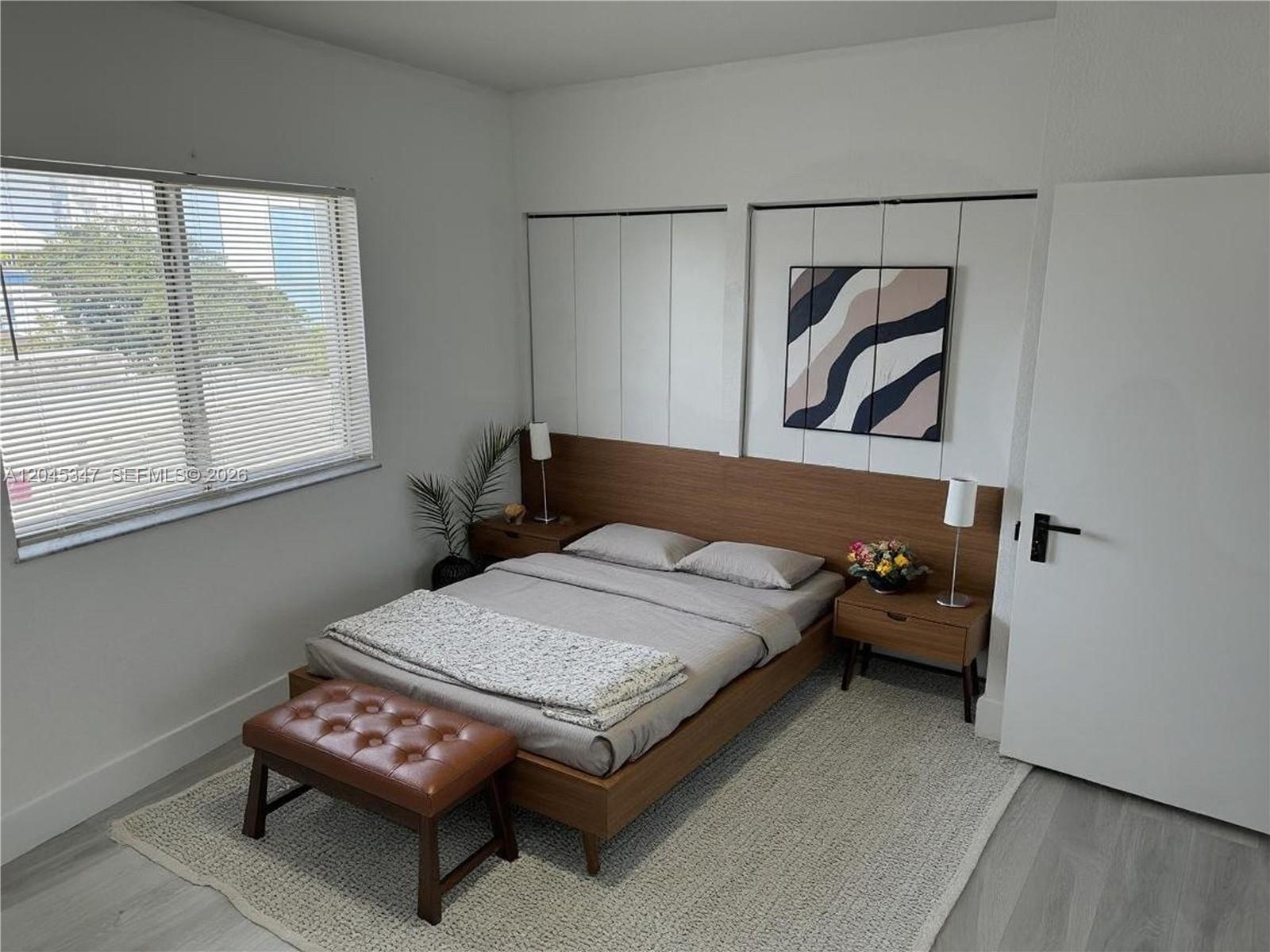 A bedroom features a wooden bed frame, matching nightstands, a tufted bench, and white closets — 36 NW 6th Ave # 601, Miami FL 33128, MIAMI, FL