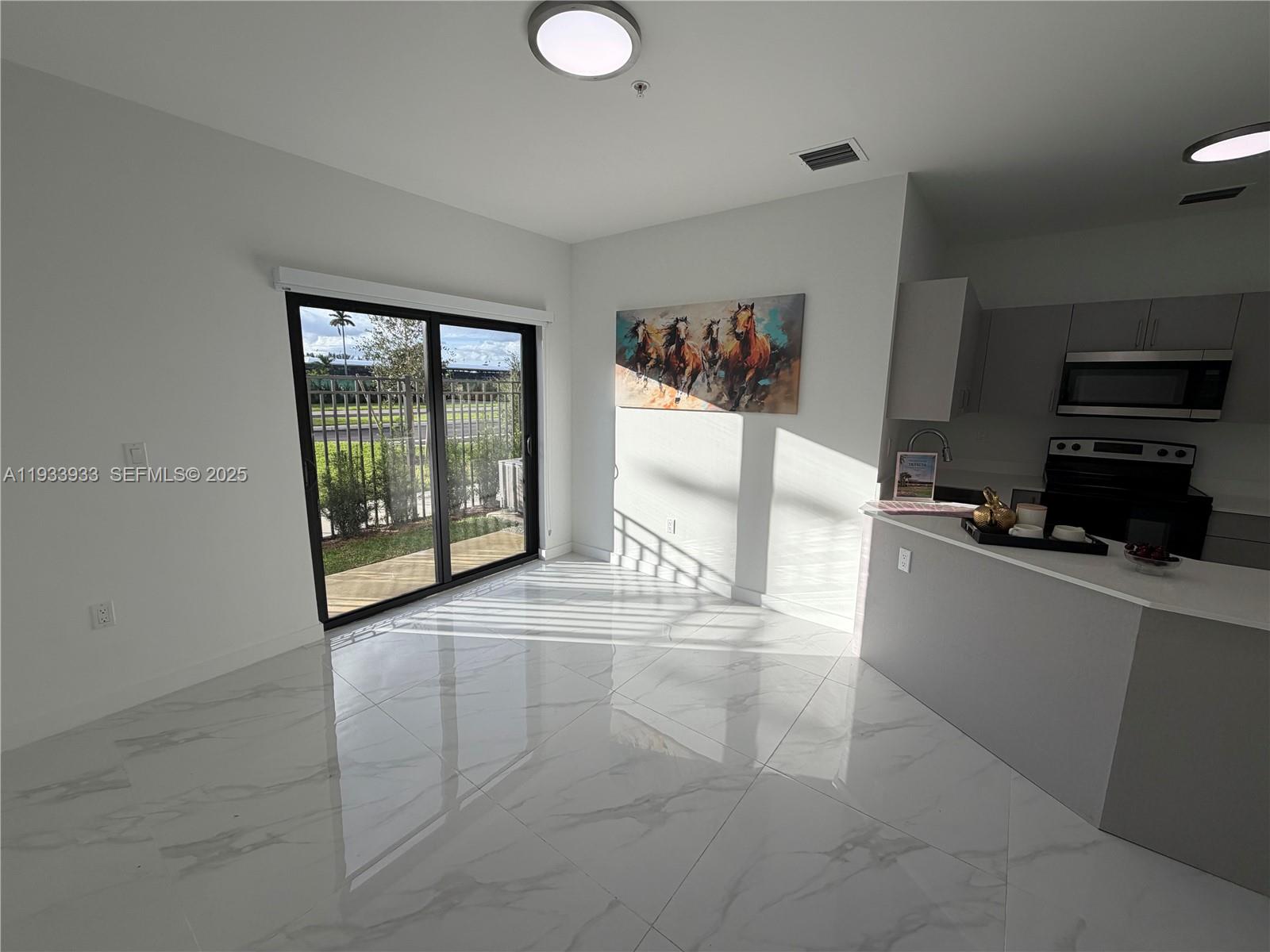 A bright dining area features white marble tile floors, a sliding glass door, and wall art — 2308 E 4th ave # 208, Hialeah FL 33013, HIALEAH, FL