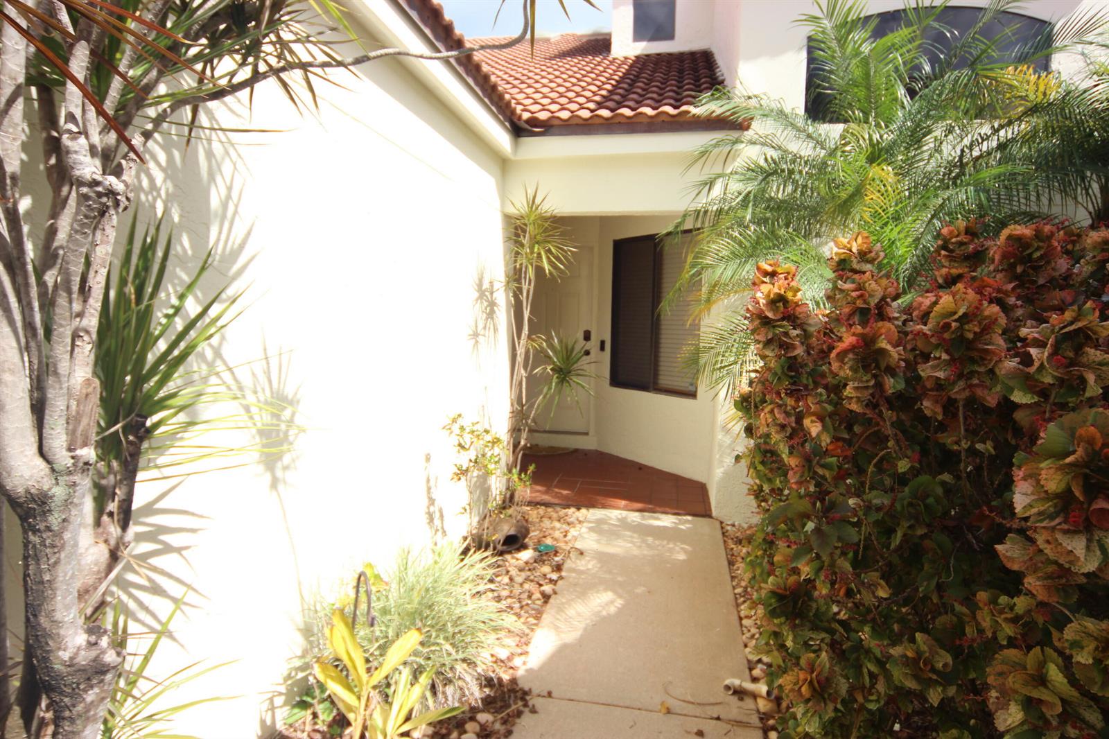 A concrete walkway leads to the front entrance of a house with tropical landscaping — 508 Sea Oats Drive # 4, Juno Beach FL 33408, JUNO BEACH, FL